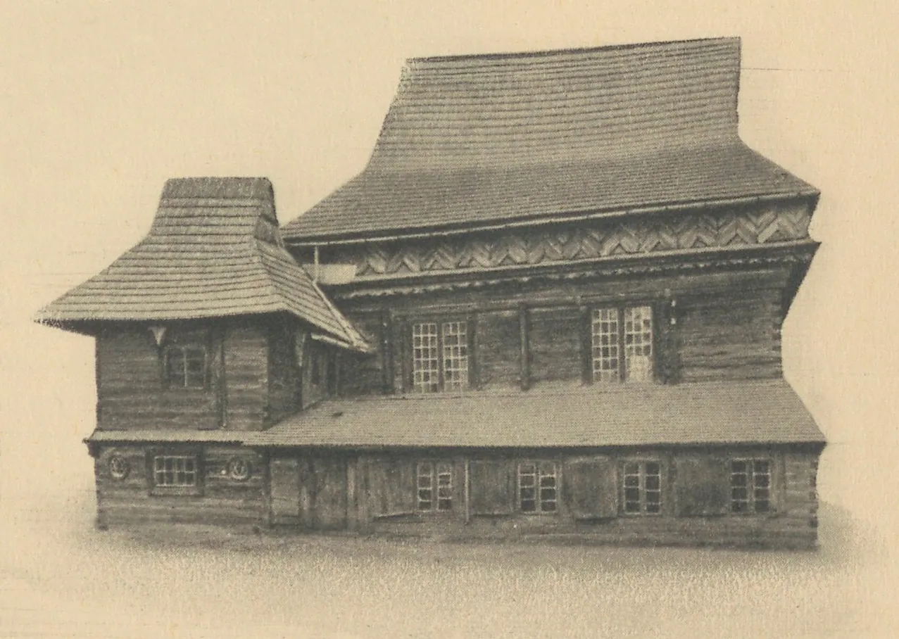 Sepia photograph of the synagogue with a steep main roof decorated with zig-zag friezes, a pavilion roof at left and a lean-to along the ground floor.