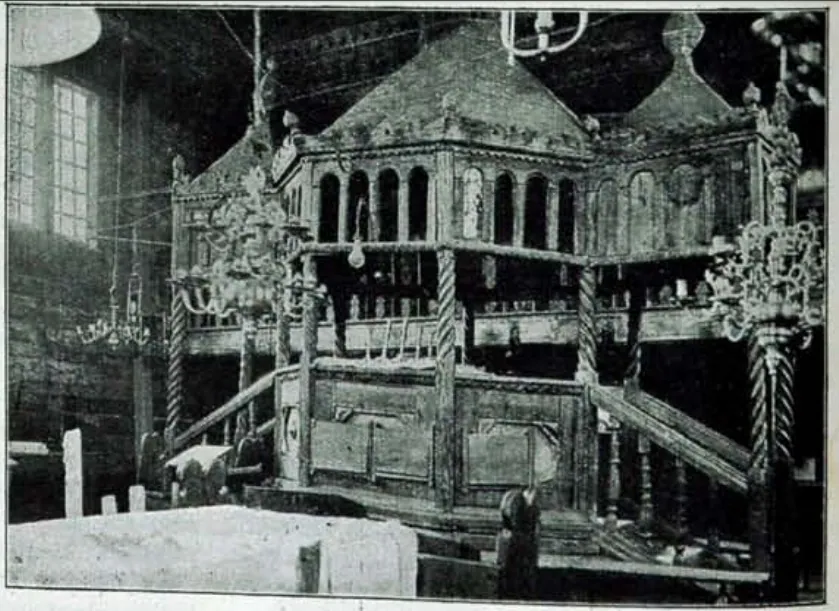 Black-and-white interior photograph of the carved octagonal bimah with twisted columns, arcades and a domed canopy, chandeliers at both sides.