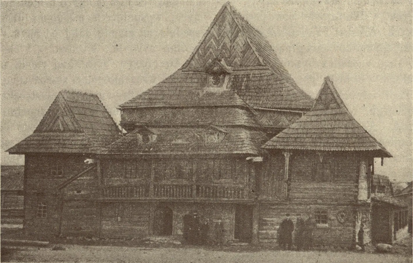 Sepia photograph of the synagogue from the front, a tall central roof flanked by pyramid-roofed corner pavilions over a galleried lower storey.