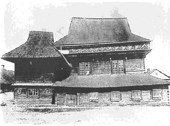 Black-and-white photograph of the timber synagogue with a steep main roof, a smaller pavilion roof at left and a long lower storey with windows.